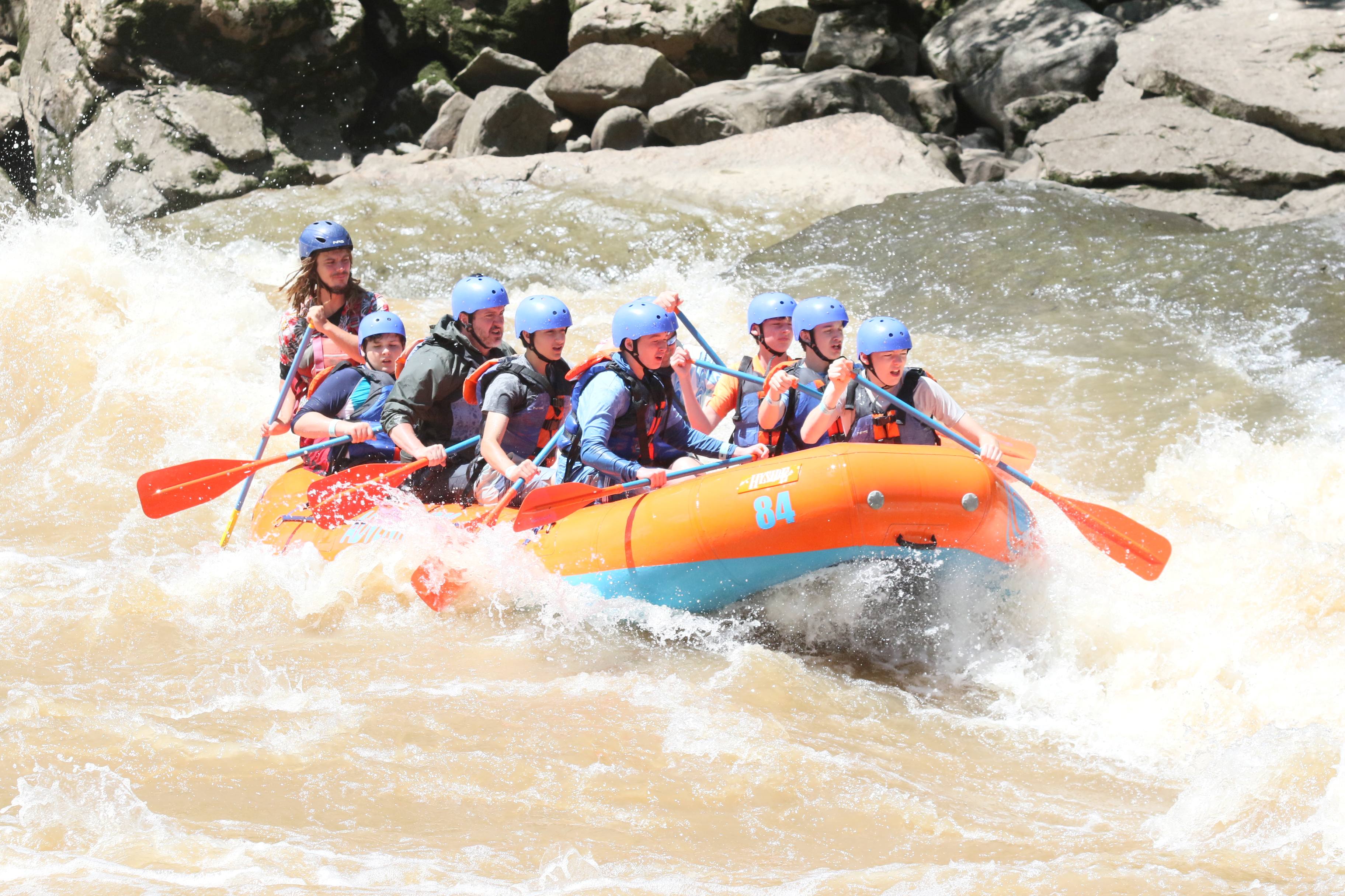 A close view of Scouts in a whitewater raft on the New River, with paddles raised and river gorge scenery around them, creating a lively and energetic high-adventure atmosphere.