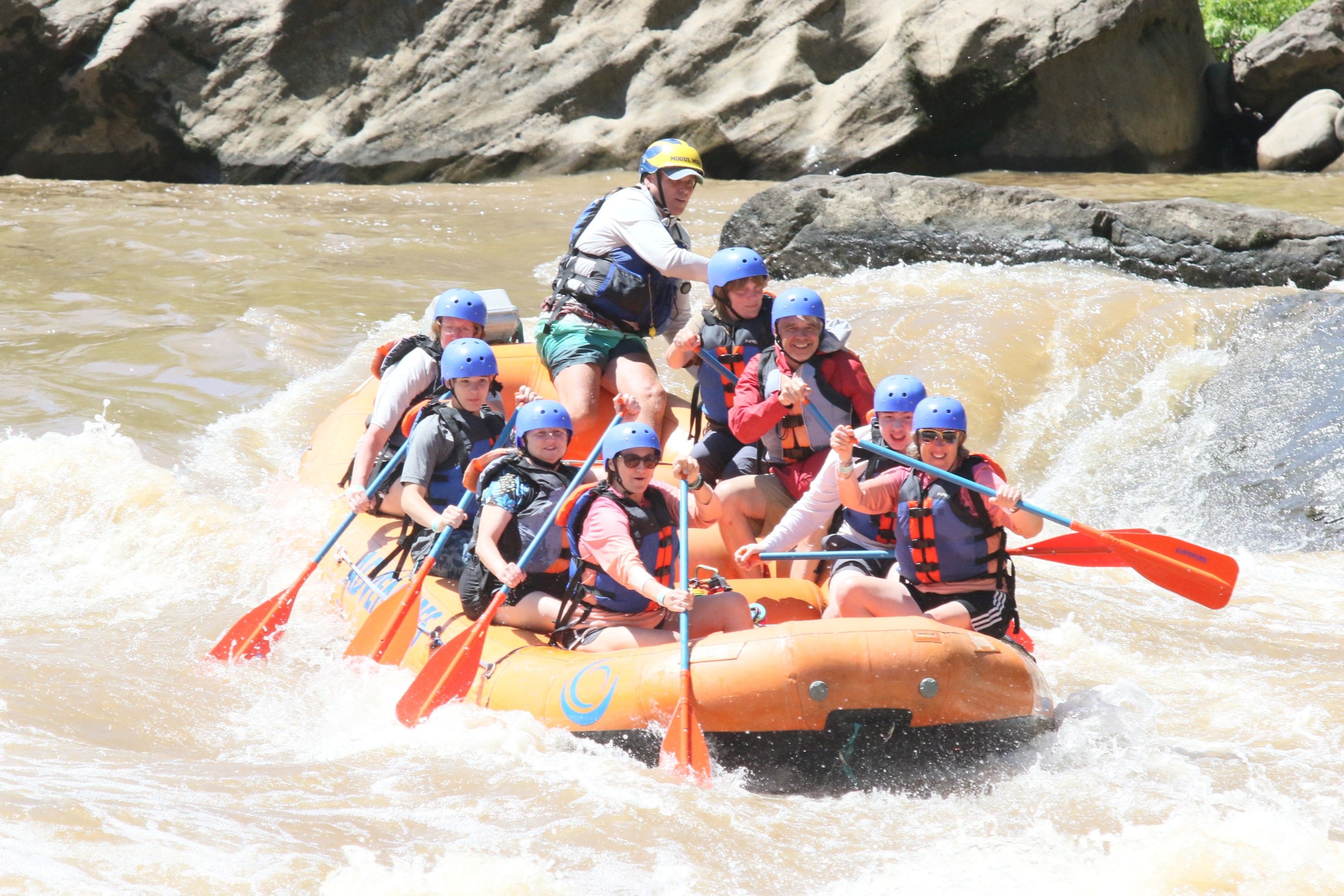 Scouts and advisors on a rafting trip in a scenic West Virginia river gorge, with life jackets, paddles, and forested mountains in the background, conveying excitement, teamwork, and adventure.