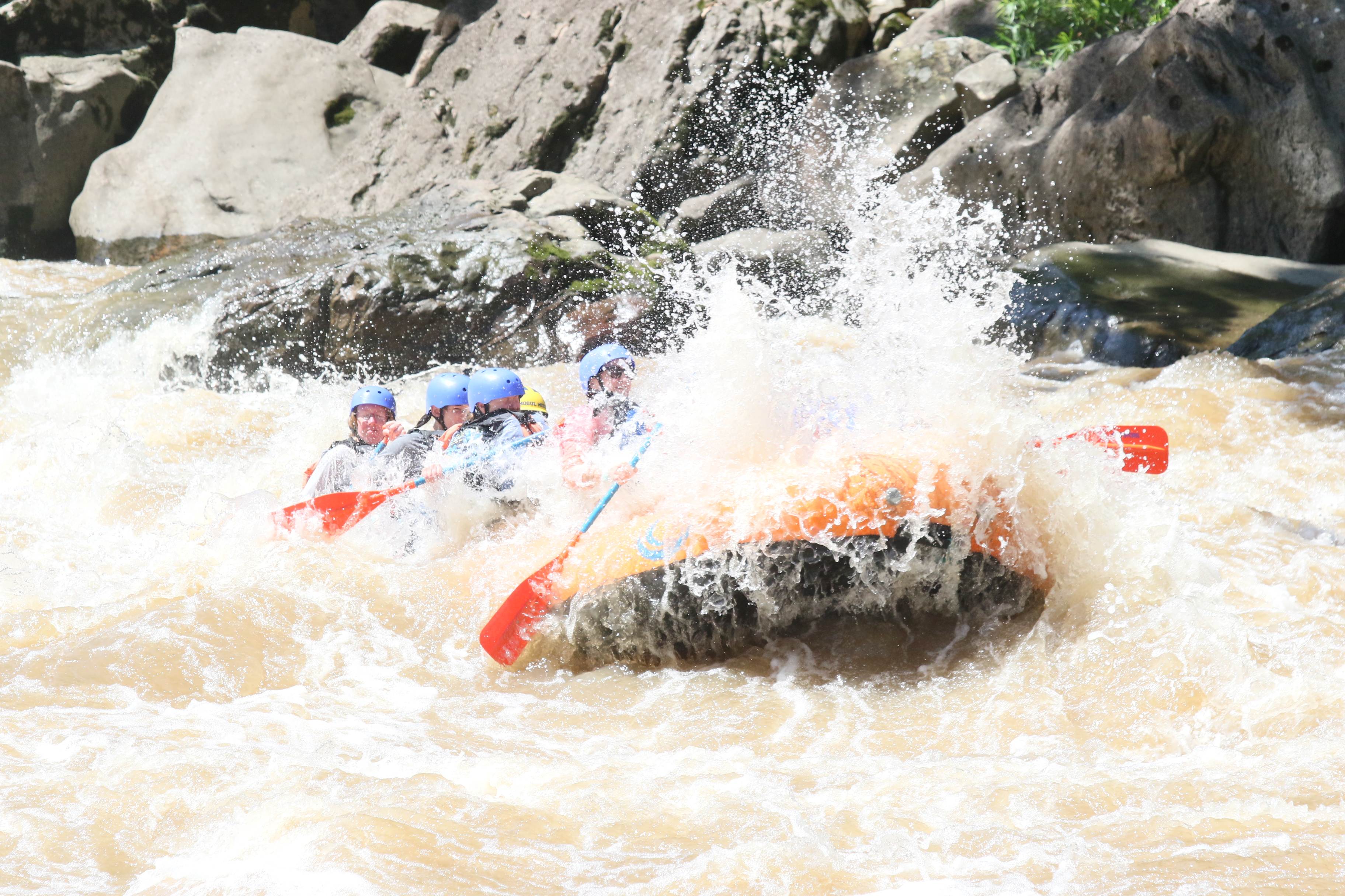 Scouts and advisors enjoying a whitewater rafting experience in a dramatic river valley, surrounded by steep cliffs, wooded slopes, and a strong sense of camaraderie and adventure.