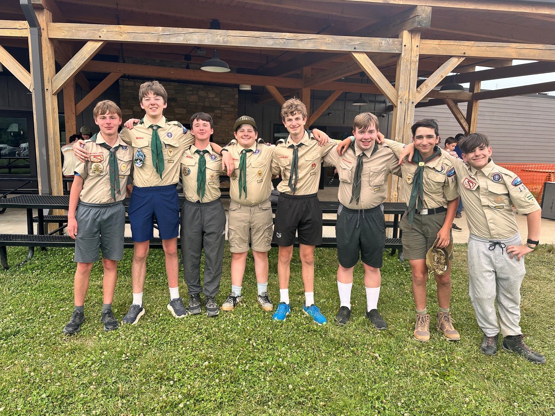 A group of Troop 135 Scouts and adult advisors standing together outdoors in a scenic mountain setting, wearing scouting gear and smiling with pride and excitement as they celebrate a successful Summit Bechtel trip.